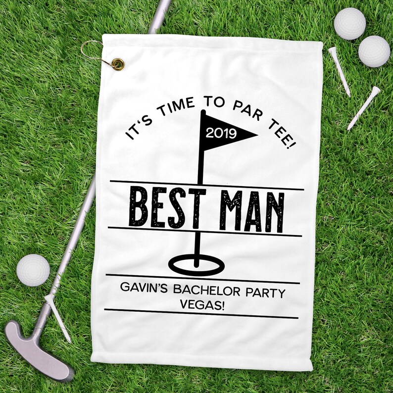 May include: White golf towel with black text: "IT'S TIME TO PAR TEE!" above a flag with "2019" and "BEST MAN" below. The text "GAVIN'S BACHELOR PARTY VEGAS!" is at the bottom. Golf balls, tees, and a putter are on the green grass.