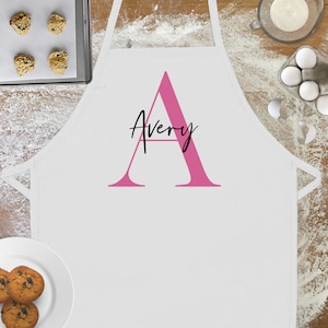 May include: White apron with a pink letter A and the name Avery written in black script.