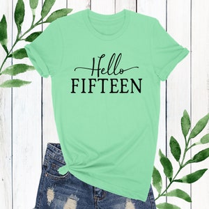 May include: A light green t-shirt with the text "Hello Fifteen" in black lettering.