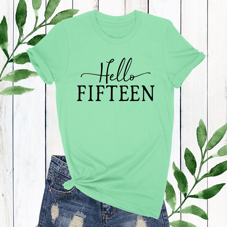 May include: A light green t-shirt with the text "Hello Fifteen" in black lettering.