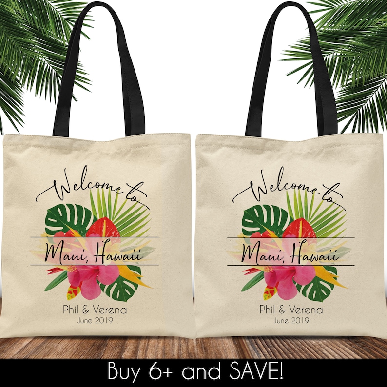 Puede incluir: Dos bolsas de lona blancas con asas negras. Las bolsas presentan un dise&ntilde;o floral tropical con el texto "Bienvenido a Maui, Haw&aacute;i" y los nombres "Phil & Verena" y la fecha "junio de 2019".