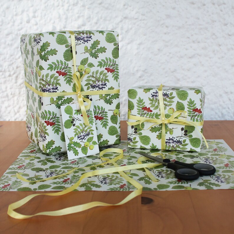 May include: Two wrapped gifts with botanical-themed wrapping paper featuring green leaves, red berries, and yellow accents. The gifts are tied with yellow ribbon and a matching gift tag. A pair of scissors and wrapping paper are also visible.
