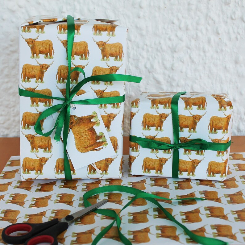 May include: Two wrapped gifts with white paper featuring a repeating pattern of brown Highland cows. The gifts are tied with green satin ribbon. A gift tag with a Highland cow illustration is attached to one package. Scissors and wrapping paper are also visible.