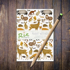 May include: A pocket notebook with a white cover adorned with illustrations of woodland creatures such as deer, foxes, and rabbits. A pencil with a green eraser lies across the notebook. The notebook has the text "Pocket Notebook" and "36 recycled plain pages".