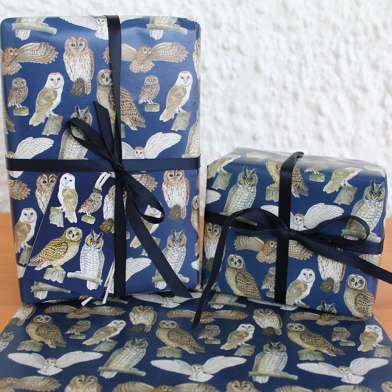 May include: Two wrapped gifts and a sheet of wrapping paper featuring a navy blue background with various owl illustrations in shades of brown, white, and tan. The gifts are tied with dark blue ribbons. The owls are depicted in different poses.