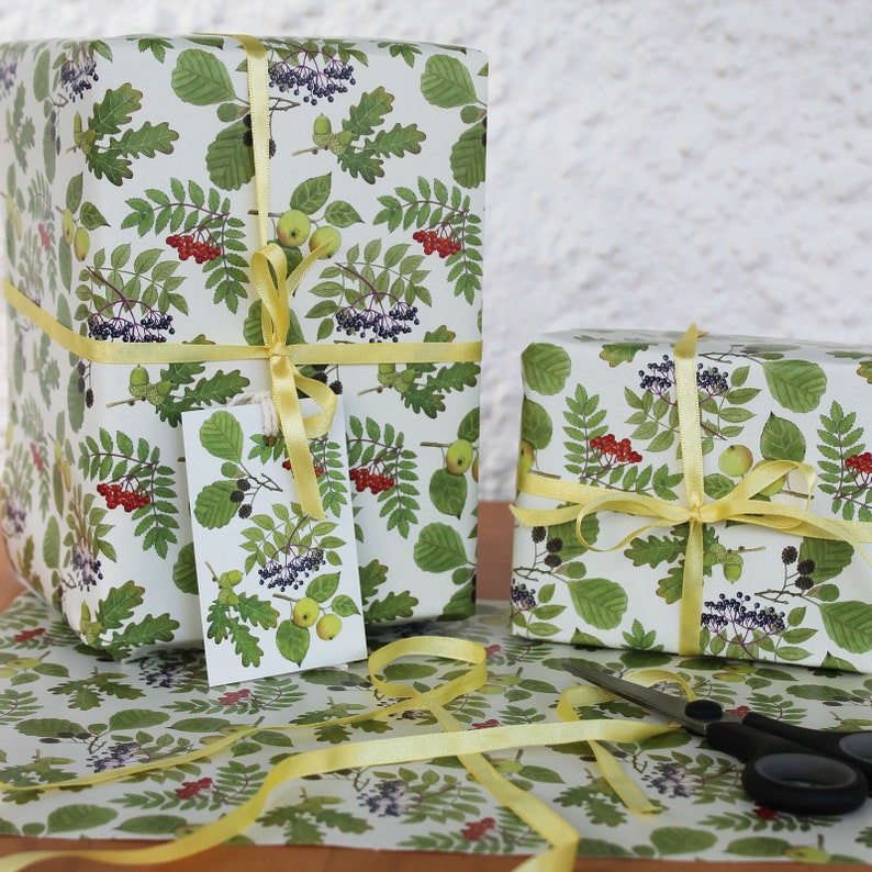 May include: Two wrapped gifts with botanical-themed wrapping paper featuring green leaves, red berries, and yellow ribbons. A matching gift tag is attached to one package. Scissors and extra ribbon are also visible.