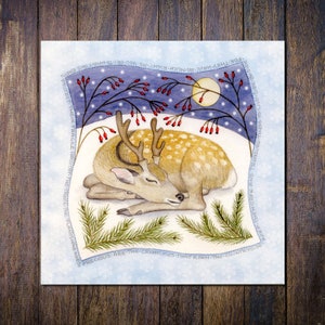 May include: A watercolour illustration of a sleeping deer with antlers, set in a snowy landscape under a full moon. The deer has brown spots and is surrounded by pine branches and berries. Text around the border reads: "Protect their fragile habitat..."