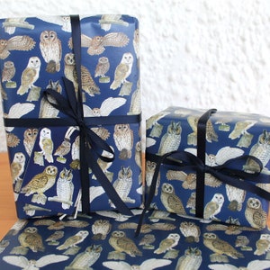 May include: Gift boxes wrapped in navy blue paper featuring a repeating pattern of various owl illustrations in shades of brown, white, and gray. The boxes are tied with dark blue ribbon, creating a decorative presentation. The theme is gift wrapping.