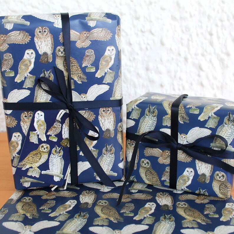 May include: Gift boxes wrapped in navy blue paper featuring a repeating pattern of various owl illustrations in shades of brown, white, and gray. The boxes are tied with dark blue ribbon, creating a decorative presentation. The theme is gift wrapping.