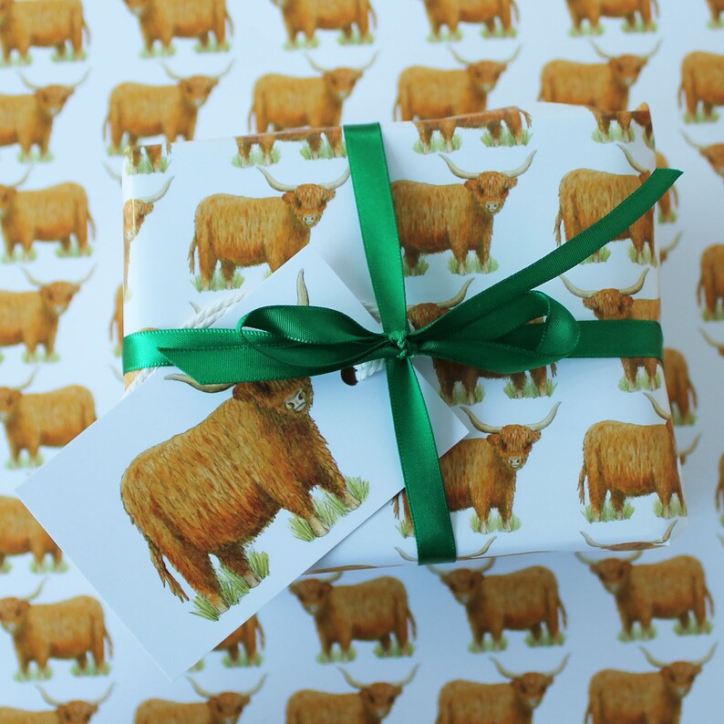 May include: A wrapped gift with a white background featuring a repeating pattern of brown Highland cows. The gift is tied with a green ribbon and a matching tag. The tag and wrapping paper have the same cow illustration.
