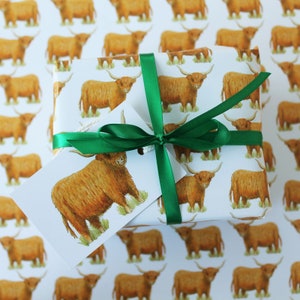 May include: A wrapped gift with white paper featuring a repeating pattern of brown Highland cows. The gift is tied with a green ribbon and a matching tag with a cow illustration. The background is the same patterned paper.