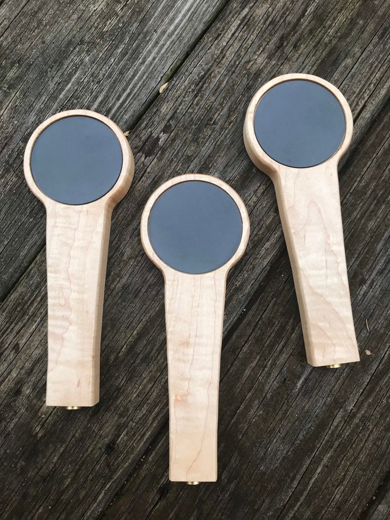 Puede incluir: Tres tiradores de cerveza de madera con insertos circulares negros. Los tiradores est&aacute;n hechos de madera de arce con un acabado natural.