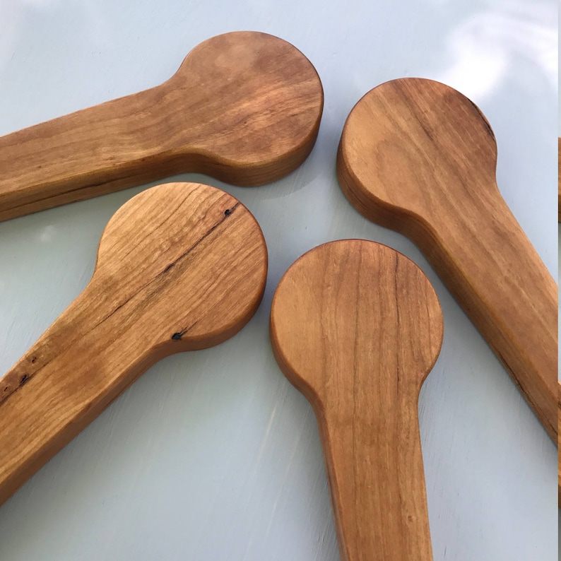 Puede incluir: Cuatro tapones de botella de madera con una parte superior redondeada y un mango largo. Los tapones son de madera marr&oacute;n claro con un acabado natural.