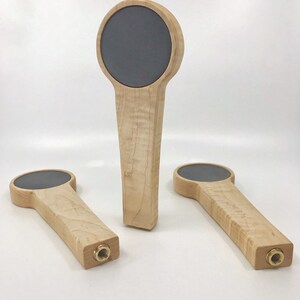 Puede incluir: Tres tiradores de cerveza de madera con una superficie redonda, gris, de estilo pizarra en la parte superior. Los tiradores est&aacute;n hechos de madera de arce con un acabado natural.
