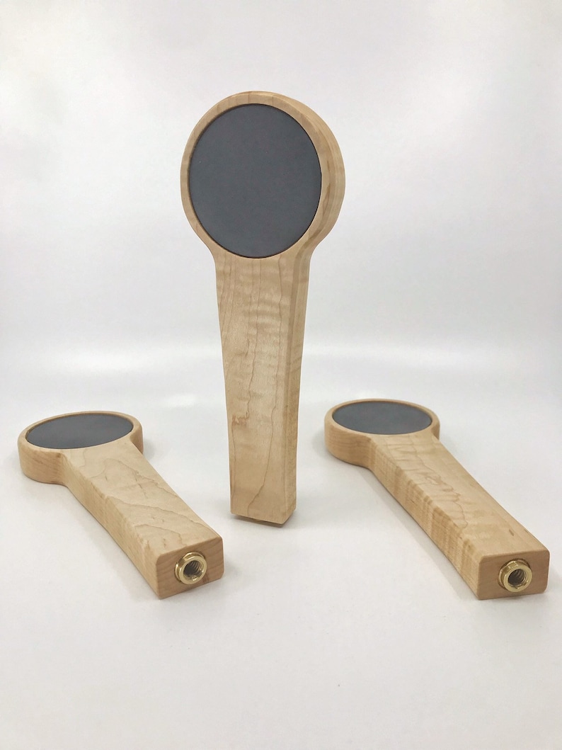 Puede incluir: Tres tiradores de cerveza de madera con una superficie redonda, gris, de estilo pizarra en la parte superior. Los tiradores est&aacute;n hechos de madera de arce con un acabado natural.