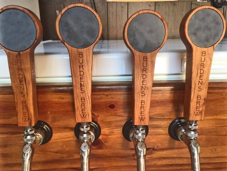 Puede incluir: Cuatro tiradores de cerveza de madera con tapas de pizarra negra. Cada tirador est&aacute; grabado con el texto "Burdens Brew".