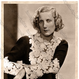 May include: A black and white portrait of a woman with blonde hair wearing a lace-trimmed blouse. The woman is smiling and looking at the camera. The image is signed "Gerald Markhel" in the bottom right corner.