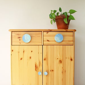 May include: A light wood cabinet with two drawers and two doors. The cabinet has blue and white painted round knobs on the drawers and doors.