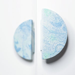 May include: Two half-circle cabinet knobs with a light blue and white marbled design.