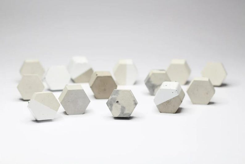 May include: A collection of small, hexagonal concrete paperweights in shades of grey and white. The paperweights have a speckled, textured surface.