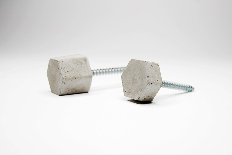 May include: Two concrete hexagon-shaped knobs with silver screws. The knobs are a light grey colour and have a rough texture.