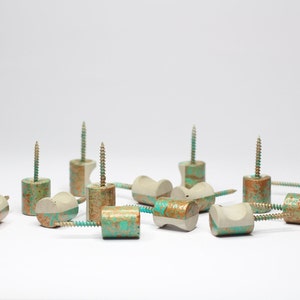 Pode incluir: Um grupo de 12 ganchos decorativos feitos de concreto com acabamento turquesa e cobre. Os ganchos são projetados para serem usados para pendurar itens em uma parede.