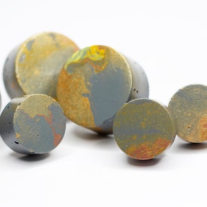 May include: A group of six round, grey concrete coasters with a marbled pattern of gold and orange paint.