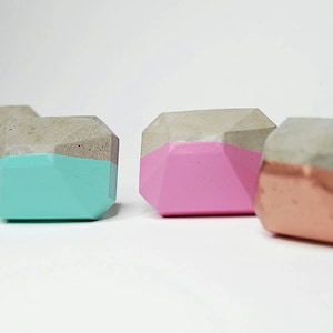 Puede incluir: Cuatro tiradores de cajones geométricos de hormigón con un acento pintado. Los tiradores son de color plateado, turquesa, rosa y cobre.