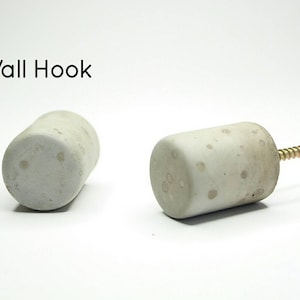 May include: A grey concrete wall hook with a brass screw. The hook is cylindrical and has a rough, textured surface.