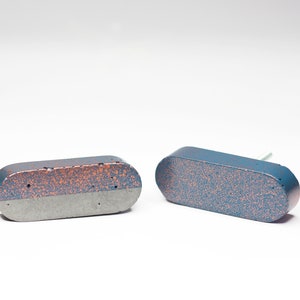 May include: Two oval-shaped concrete drawer pulls with a speckled blue and copper finish. One pull has a grey base, while the other is entirely blue.