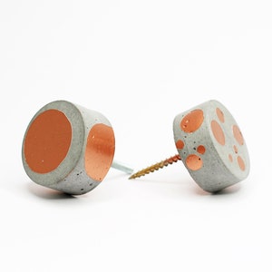 Könnte beinhalten: Zwei graue Betonknauf mit kupferfarbenen Punkten. Jeder Knauf hat eine Schraube.