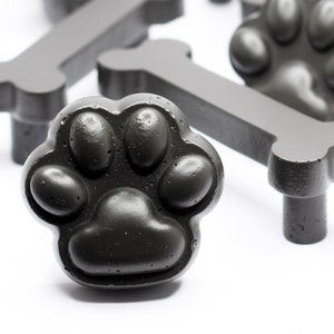 Könnte beinhalten: Ein Satz schwarzer Schrankknöpfe in Form von Pfotenabdrücken und Knochen. Die Knöpfe sind aus einem strukturierten Material gefertigt und haben eine matte Oberfläche.