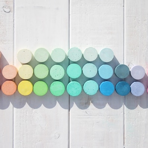 Peut inclure: Une collection d'objets ronds colorés disposés en dégradé. Les couleurs varient du rouge et orange chauds aux bleus, verts et roses froids. Les objets sont posés sur une surface en bois blanc.