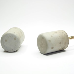 May include: Two concrete cylinder door knobs with a speckled finish. One knob has a gold screw attached.
