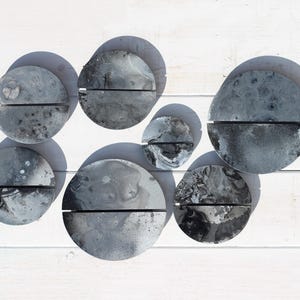 Può includere: Una composizione di sette elementi decorativi astratti grigi e neri per pareti. Ogni pezzo è un semicerchio con una linea orizzontale al centro. I pezzi hanno un effetto marmorizzato e sono disposti su una superficie di legno bianco.