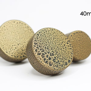 May include: Three round, 40mm, gold-colored bottle stoppers with a crackled finish. The stoppers have a black base.