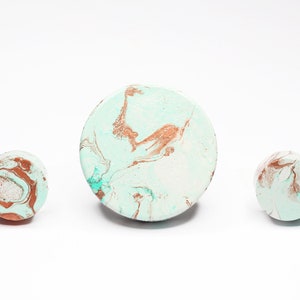 Pode incluir: Três  tapetes redondos decorativos com um design de mármore em tons de branco, turquesa e cobre.