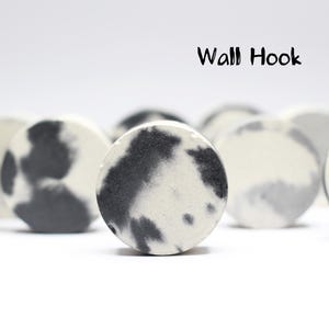 Op de afbeelding: Een verzameling ronde wandhaken met een gespikkeld zwart-wit ontwerp. De haken zijn in een rij gerangschikt, met de tekst "Wall Hook" in het zwart erboven. De haken zijn gemaakt van een stevig materiaal en staan tegen een witte achtergrond.
