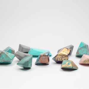 Może przedstawiać: Kolekcja małych, geometrycznych, diamentowych obiektów w różnych kolorach, w tym turkusowym, szarym, różowym i złotym. Obiekty mają fakturowaną, marmurową powierzchnię.
