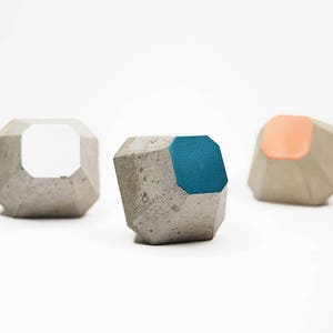 May include: Three concrete geometric shapes with different coloured accents. The shapes are a light grey with a white, teal, and peach accent.
