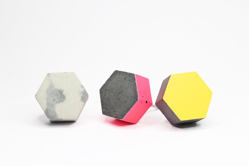 May include: Three hexagonal concrete objects, one is grey, one is grey with a pink side, and one is grey with a yellow side.