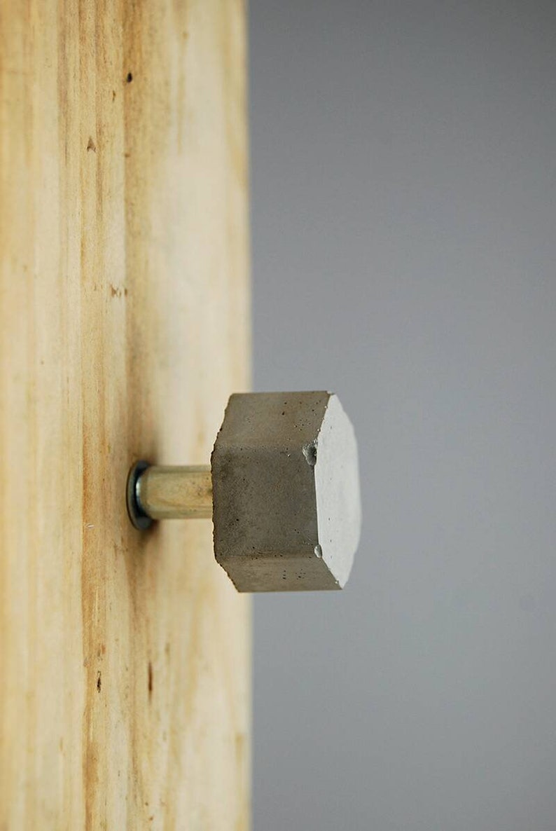 May include: A grey concrete door knob with a silver metal rod attached to a wooden surface.