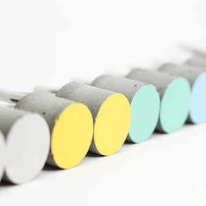 May include: A row of ten concrete knobs in a variety of colours, including yellow, green, blue, and grey. The knobs are arranged in a gradient from yellow to grey.