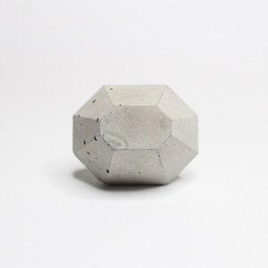 Peut inclure: Une forme géométrique en béton gris avec une texture rugueuse. La forme est un dodécaèdre, une figure à 12 faces.