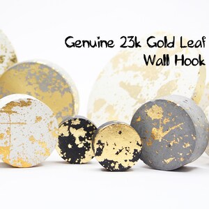 May include: A collection of decorative wall hooks with a gold leaf design. The hooks are in various shapes and sizes, with a mix of white, gray, and black bases. The text "Genuine 23k Gold Leaf Wall Hook" is visible.