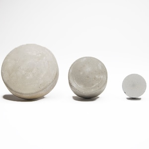Könnte beinhalten: Drei Betonkugeln in verschiedenen Größen, die größte ist etwa so groß wie eine Grapefruit, die mittlere etwa so groß wie eine Limette und die kleinste etwa so groß wie eine Murmel.