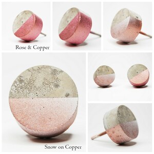 May include: Two pairs of concrete earrings with a half-circle design. One pair is painted with a light pink colour on the bottom half of the circle, and the other pair is painted with a light grey colour on the top half of the circle. The earrings are labelled "Rose & Copper" and "Snow on Copper".