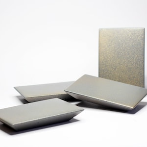 May include: Four rectangular ceramic dishes in a light gray color with a subtle speckled texture. The dishes are arranged in a pyramid shape on a white surface.