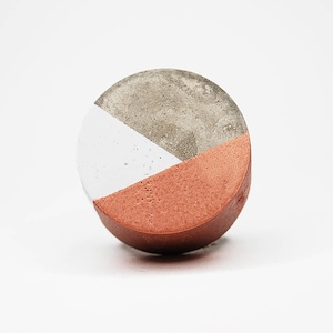 Könnte beinhalten: Ein runder Untersetzer aus Beton mit einem Farbschema in Weiß, Grau und Kupfer. Der Untersetzer besteht aus drei Teilen in verschiedenen Farben.