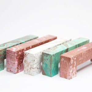 May include: Five concrete drawer pulls in various colours, including green, pink, and white. Each pull has a marbled pattern and a rectangular shape.